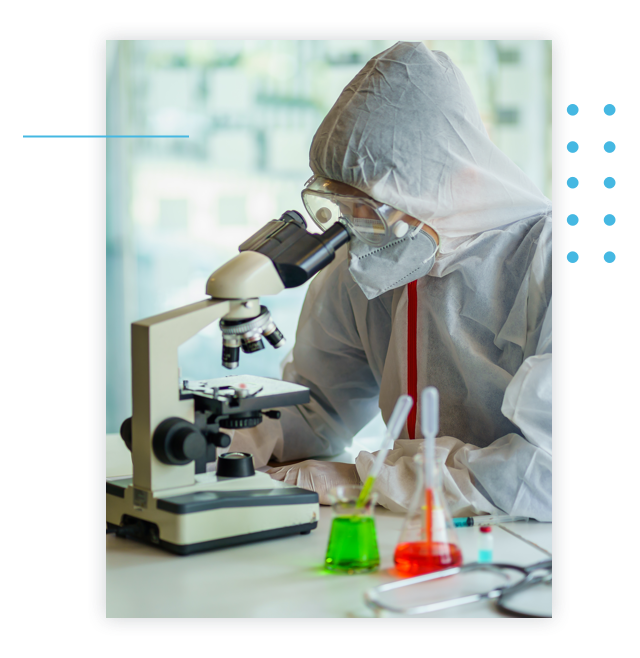 A scientist dressed in protective gear looks in a microscope.