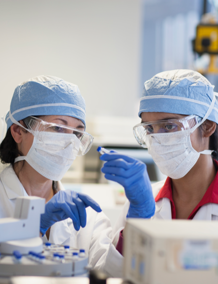 Two scientists dressed in protective gear examine a sample.