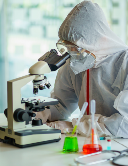 A scientist dressed in protective gear looks in a microscope.